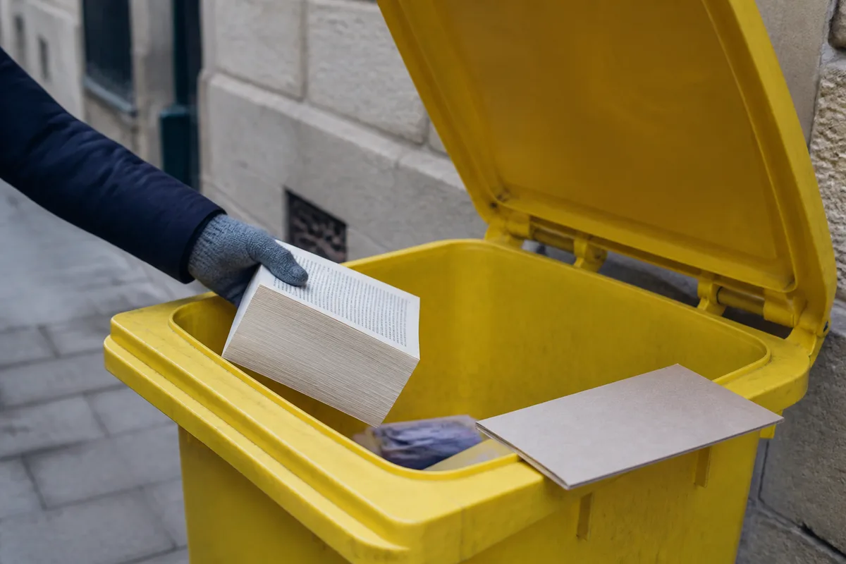 Bac de tri jaune recevant des pages de livres séparées de leur couverture